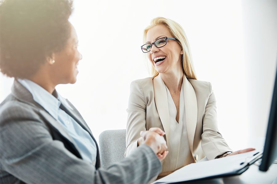 About Our Agency - Closeup Portrait of Two Smiling Business Women in the Office Shaking Hands