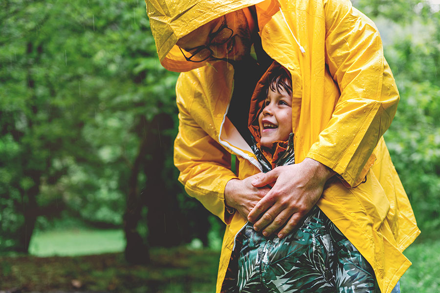 Contact - Closeup Portrait of a Father in a a Raincoat Hugging His Smiling Young Son as They Both Stand in the Rain in a Park
