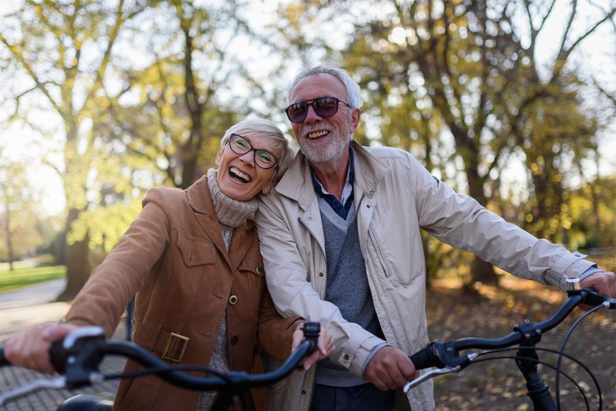 Employee Benefits - Portrait of a Cheerful Mature Couple Having Fun Riding Their Bikes in the Park During the Fall