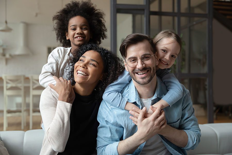 Personal Insurance - Closeup Portrait of a Cheerful Young Family with Two Kids Sitting in a Modern Living Room